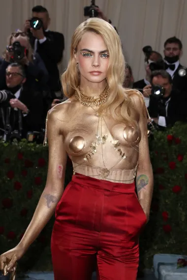 Cara Delevingne je ove godine odlučila šokirati javnost svojom pojavom na Met Gali. Naime, pojavila se u toplesu, bez ikakvog komada odjeće na gornjem dijelu tijela, a grudi i cijeli torzo bili su joj obojeni u zlatnu šljokastu boju. Tako je Sama Cara postala zlatna statua, a cijeli look je zaokružila crvenim hlačama visokog struka i brojnim zlatnim ukrasima u vidu narukvica, ogrlica i štapa za hodanje. Zanimljivo je da je nosila i popularne Versace platforme u crvenoj boji, a cijeli njezin look potpisala je modna kuća Dior. 
