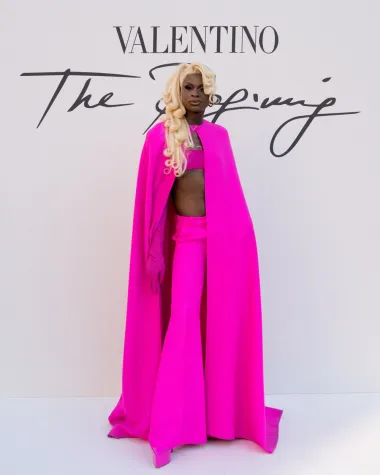 Slavna američka drag queen Symone na reviju je stigla u trapez ružičastim hlačama, platformama ultra kratkom topu, dugačkim rukavicama do iznad lakta, a outfit je upotpunila plaštem u istoj nijansi. 
