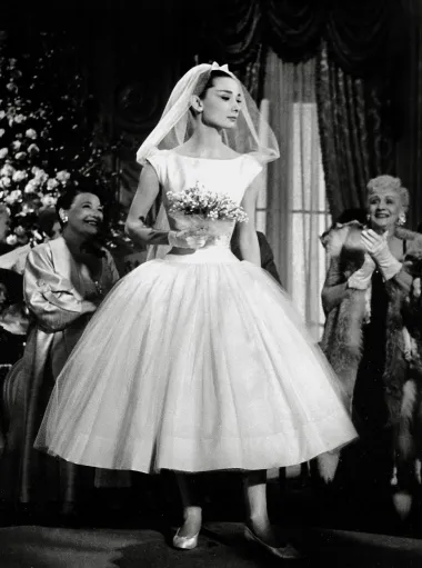 Ova malo kraća vjenčanica Huberta de Givenchyja u mjuziklu &quot;Smiješno lice&quot; naglasila je vitku figuru Audrey Hepburn i uz to je nevjerojatno razigrana i lepršava. To je idealna haljina za one mladenke koje žele uživati u plesu na svom vjenčanju.