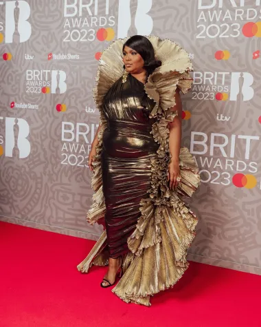 Pjevačica Lizzo nosila je raskošnu couture haljinu dizajnera Roberta Wuna. Ovaj ekstravagantni look sastojao se od metalik haljine na jedno rame, s golemim zlatnim volanima, a pjevačica je look upotpunila parom crnih sandala s remenčićima marke Pīferi.