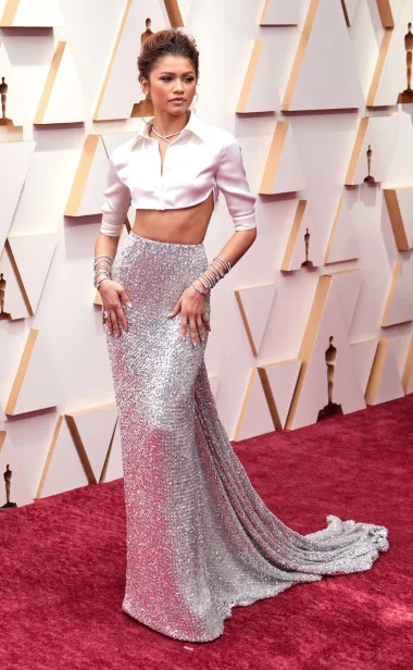 &quot;Zendaya je potpuno dominirala crvenim tepihom na Oscarima 2022. godine. Njezin dvodijelni look bio je pravo modno iznenađenje – bijela cropped košulja iz Valentino Haute Couture kolekcije uparena s večernjom suknjom ukrašenom srebrnim šljokicama. Styling je upotpunila s hrpom Bulgari Serpenti Viper narukvica od bijelog zlata, potpuno optočenih dijamantima.&quot; 