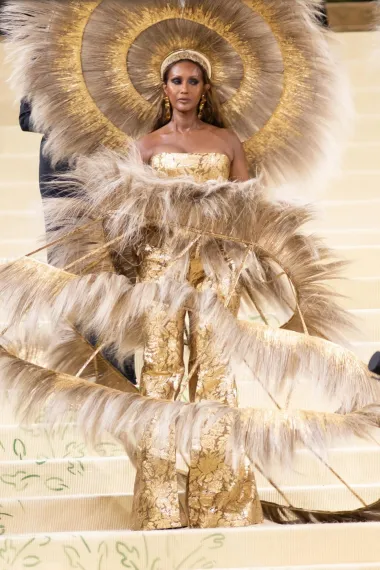 Haljina supermodela Iman zahtijevala je 400 sati izrade! Zlatna suknja nalik kavezu, ukrašena perjem, u kombinaciji s zlatnim odijelom bez rukava i ogromnim ukrasom za glavu, jednostavno je očaravajuća. Ovaj izgled, rezultat suradnje Dolce &amp; Gabbana i Harris Reeda, inspiriran je balnom kulturom iz zlatnog doba Amerike.